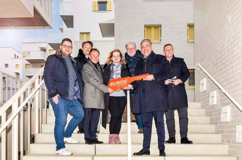 Menschengruppe, die einen figurativen Schlüssel hält und in die Kamera lacht.