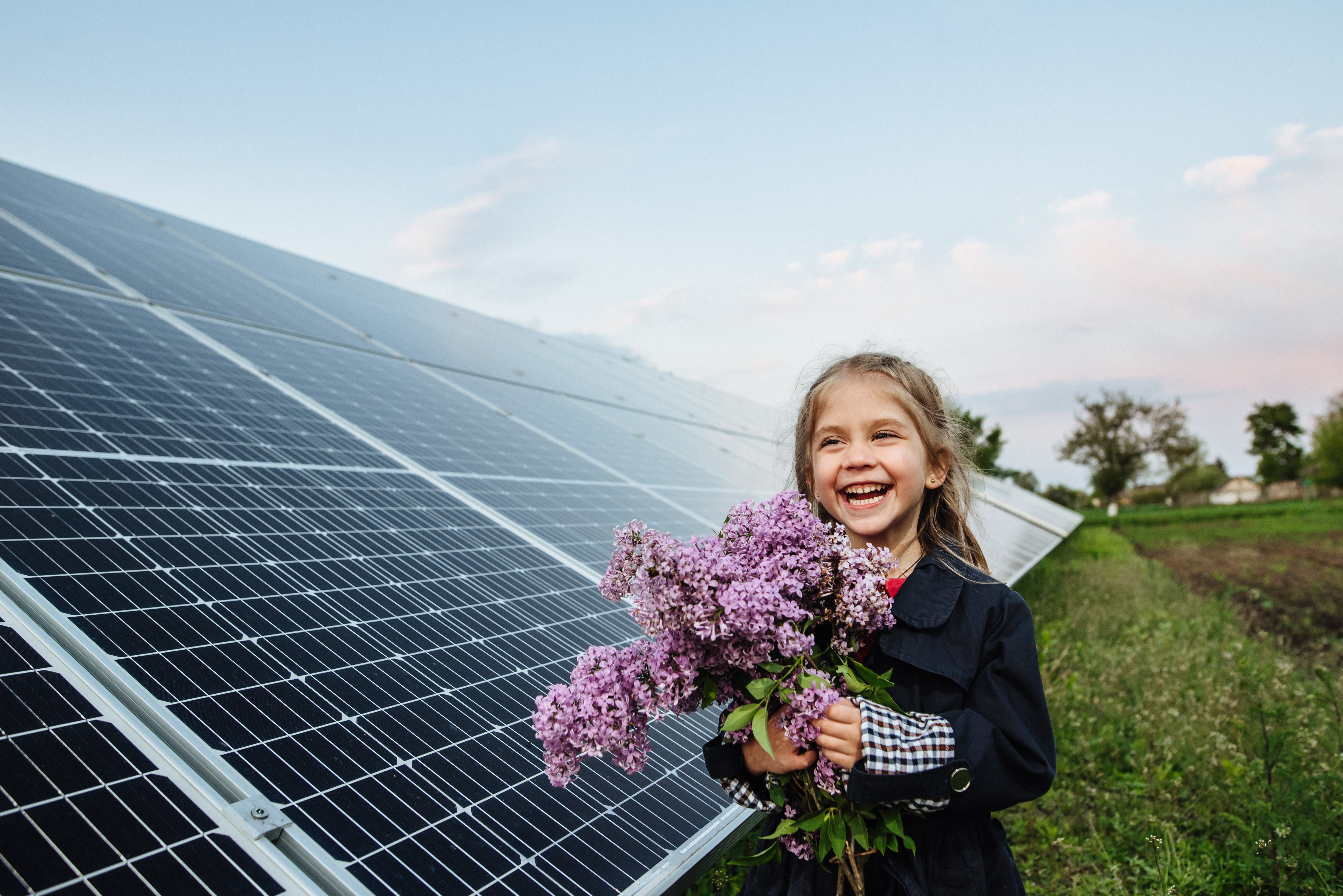 Lachendes Mädchen mit Blumenstrauss vor PV-Anlage.