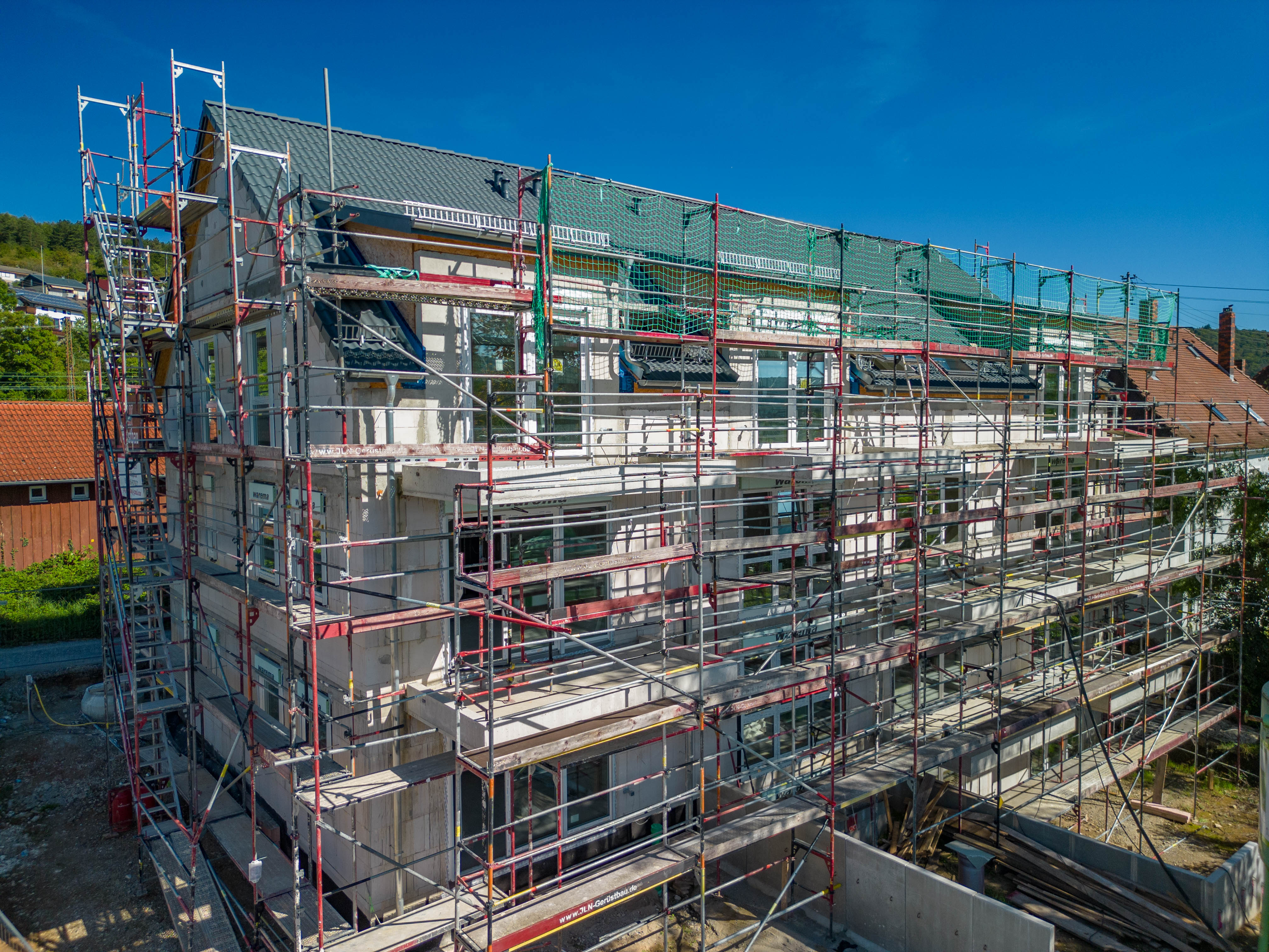 Zu sehen ist eine Drohnenaufnahme vom Projekt im Friedhofweg. Das Haus ist noch eingebaut zu diesem Zeitpunkt des Bildes. Man erkennt Balkone und Garten.