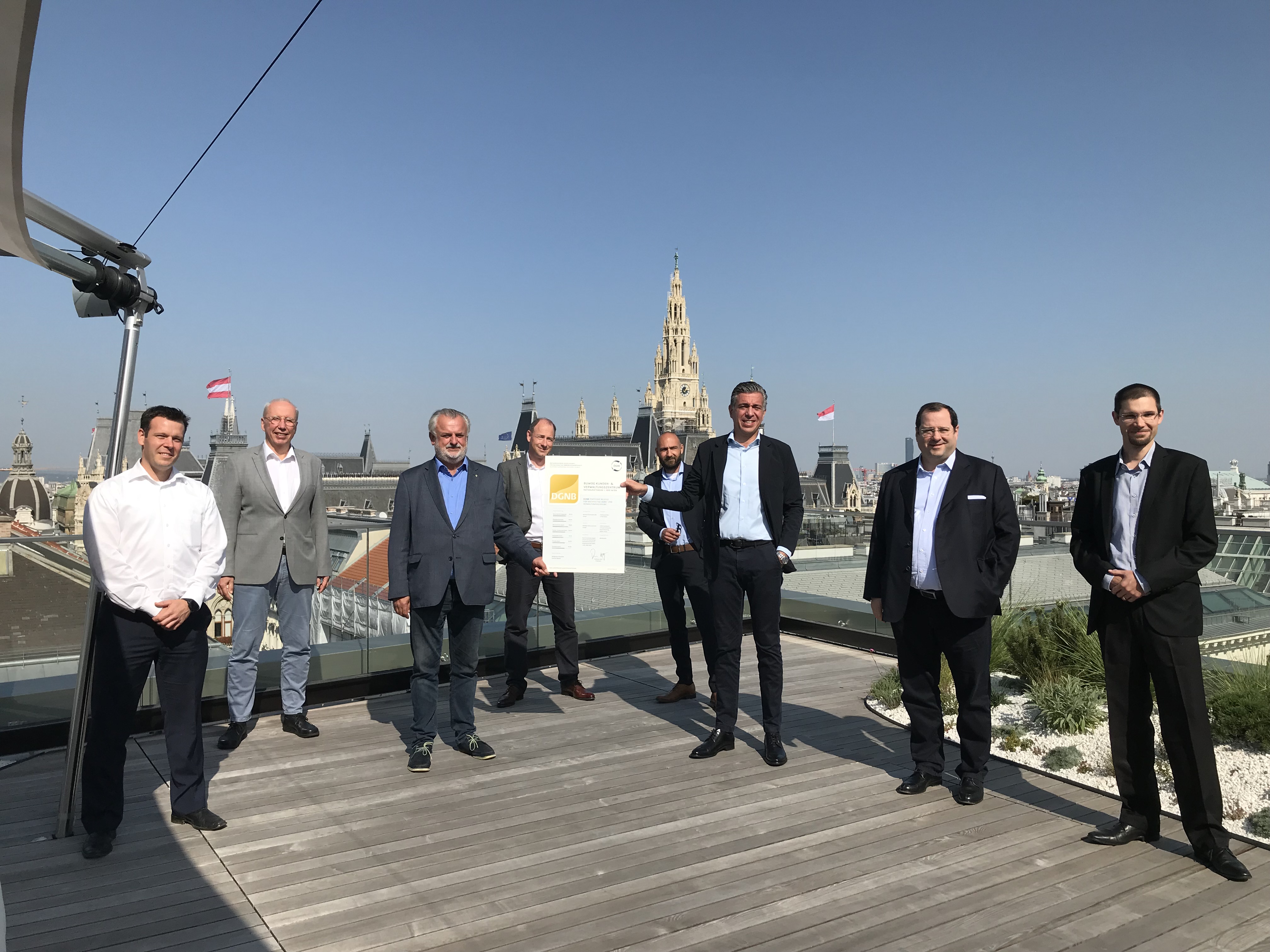 Mitarbeiter:innen stehen auf der Terrasse eines hohen Gebäudes in Wien und präsentieren ein Zertifikat