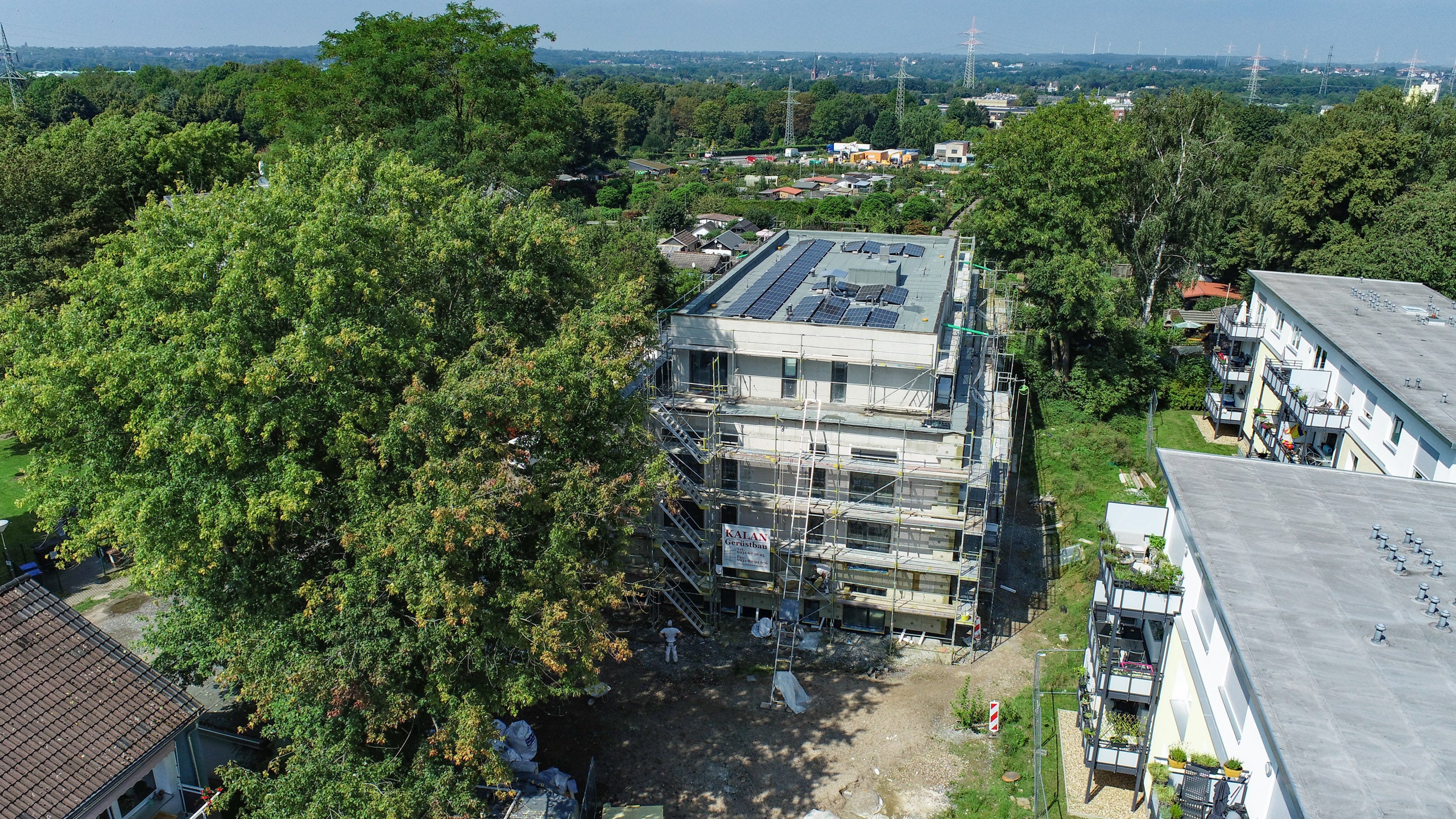 Zu sehen ist eine Drohnenaufnahme vom Projekt am Hartweg in Dortmund. Das Haus ist noch eingebaut zu diesem Zeitpunkt des Bildes. Man erkennt Balkone, den Garten und den Hof, sowie noch Bauarbeiter.